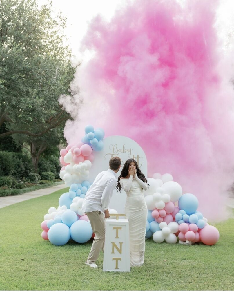 Gender reveal party Budapest - couple celebrating with pink smoke bomb and balloon arch decoration in outdoor park