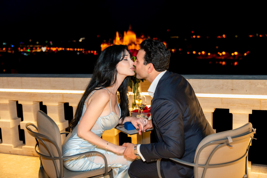 Romantic couple kissing during a candlelit dinner on a Budapest terrace with the Parliament lit up in the background